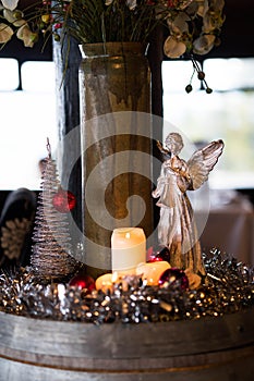 A lit up real candle with a decorative angel and a silver Christmas tree