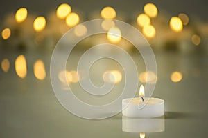 A lit white candle on a background of blurred lights