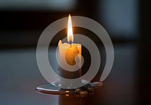A lit white candle sits on a smooth, dark surface, with melted wax pooling around its base. The