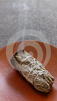 A lit white sage smudge stick on a dish.