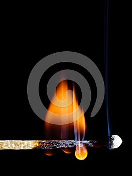 A lit wooden match flaming with an orange flame isolated on black