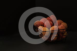 Litchi  lie in a black metal decorative basket against  black background