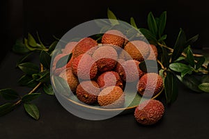 Litchi  lie on a ceramics green  plate, around a sprig with leaves on a black background