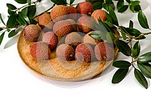 Litchi  lie on a wooden plate, around a sprig with leaves, isolated
