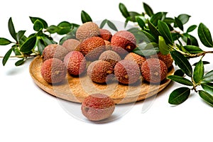 Litchi  lie on a wooden plate, around a sprig with leaves, isolated