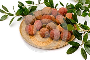 Litchi lie on a wooden plate, around a sprig with leaves on a white background