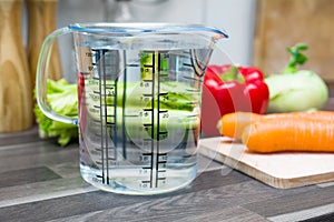 1 Liter / 1000ml / 10dl Of Water In A Measuring Cup On A Kitchen Counter With Vegetables