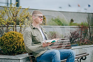 Literary Urbanite A Young with eyeglasses Man Sitting with Book in the City photo