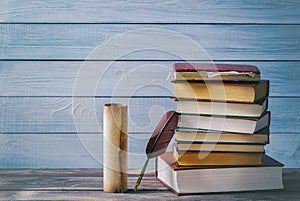 Literature concept. Brown feather near old scroll and stack of old books against blue wooden background