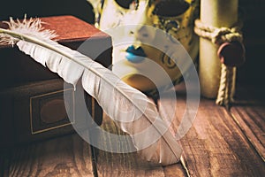 Literature concept. Feather on book near venetian mask and old scroll on wooden background