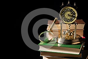 Literature concept. Magnifying glass near vintage clock on old books against black background