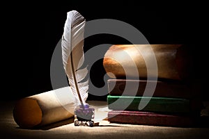 Literature concept. Old inkstand with feather near scrolls and books against black background. Dramatic light photo