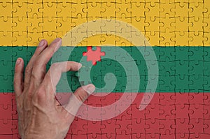 Lithuania flag is depicted on a puzzle, which the man`s hand completes to fold