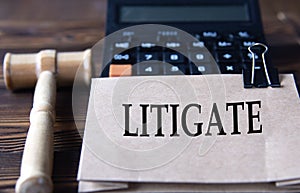 LITIGATE - word on light brown paper against the background of a calculator and a judge's gavel