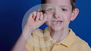 Litle caucasian boy holds a dropped milk tooth between his fingers