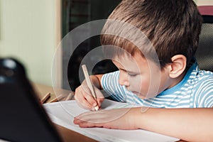 Litle child siting at desk and drawing letters album with colored pencils