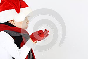 Littel boy in santa claus hat and scarf and gloves blowing snowflakes
