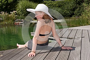 Littel girl with hat sitting at the pool and looking into the wa