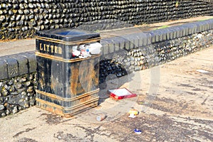 Litter bin overflowing, trash and rubbish spilling out.