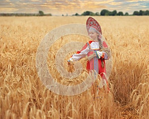 Littl girl kid in Russian national sarafan and a kokoshnik standing in a golden wheat field in summer day