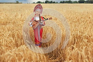 Littl girl kid in Russian national sarafan and a kokoshnik standing in a golden wheat field in summer day