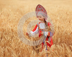 Littl girl kid in Russian national sarafan and a kokoshnik standing in a golden wheat field in summer day