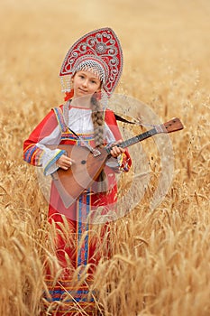 Littl girl kid in Russian national sarafan and a kokoshnik standing in a golden wheat field in summer day