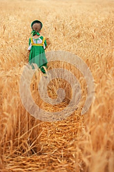 Littl girl kid in Russian national sarafan and a kokoshnik standing in a golden wheat field in summer day