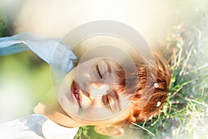 Little 7 years old smiling girl with closed eyes and stylish short haircut laying down in grass under blooming cherry tree in