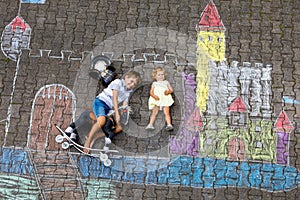 Little active kid boy and cute toddler baby girl drawing knight castle and fortress with colorful chalks on asphalt