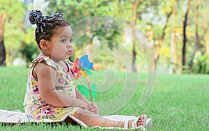 Little adorable African girl learning, doing activity, sitting for picnic, happily playing wind turbine outdoor garden in summer