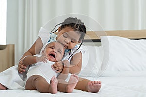 Little adorable African older sister is lulling, comforting and hugging newborn baby girl to sleep with love and care