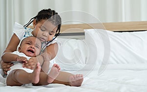 Little adorable African older sister is lulling, comforting and hugging newborn baby girl to sleep with love and care while infant
