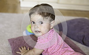 Little adorable baby girl with a toy crawling on the floor at home. Closeup indoor portrait