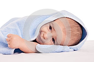 Little adorable baby lying on bed under blue towel