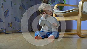 Little adorable baby takes a phone and smiles while sitting on the floor