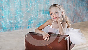 Little adorable ballerina in white tutu with old vintage suitcase in a beautiful studio.