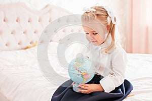 Little adorable blonde girl in school uniform and white golfs siting on a ber in her bedroom and shockes about first day in the photo