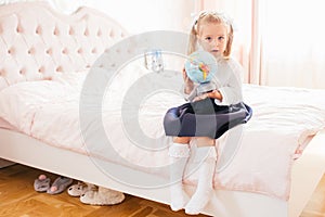 Little adorable blonde girl in school uniform and white golfs siting on a ber in her bedroom and shockes about first day in the photo