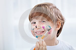 Little adorable child boy making a mess with colors on his face