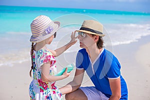 Little adorable girl applying sun cream to her father nose