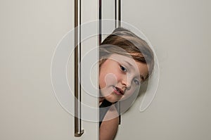 Little adorable girl child peeking out of the cabinet doors