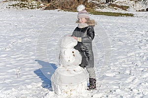 Little adorable girl child sculpts snowman from snow in winter