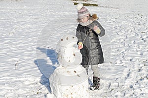 Little adorable girl child sculpts snowman from snow in winter