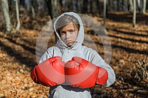 Little adorable girl child in a tracksuit, with a hood on his head, in red boxing gloves, boxing on the street in the autumn fores