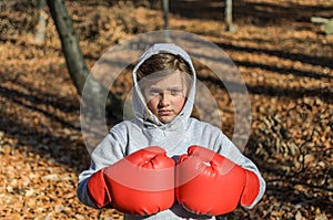 Little adorable girl child in a tracksuit, with a hood on his head, in red boxing gloves, boxing on the street in the autumn fores