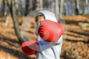 Little adorable girl child in a tracksuit, with a hood on his head, in red boxing gloves, boxing on the street in the autumn fores