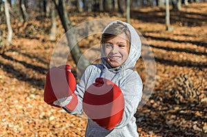 Little adorable girl child in a tracksuit, with a hood on his head, in red boxing gloves, boxing on the street in the autumn fores