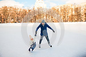 Little adorable girl with father learning to skate on ice-rink