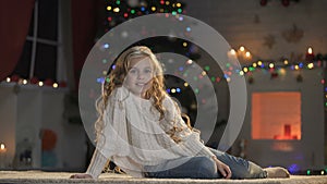 Little adorable girl on floor under decorated X-mas tree, smiling to camera